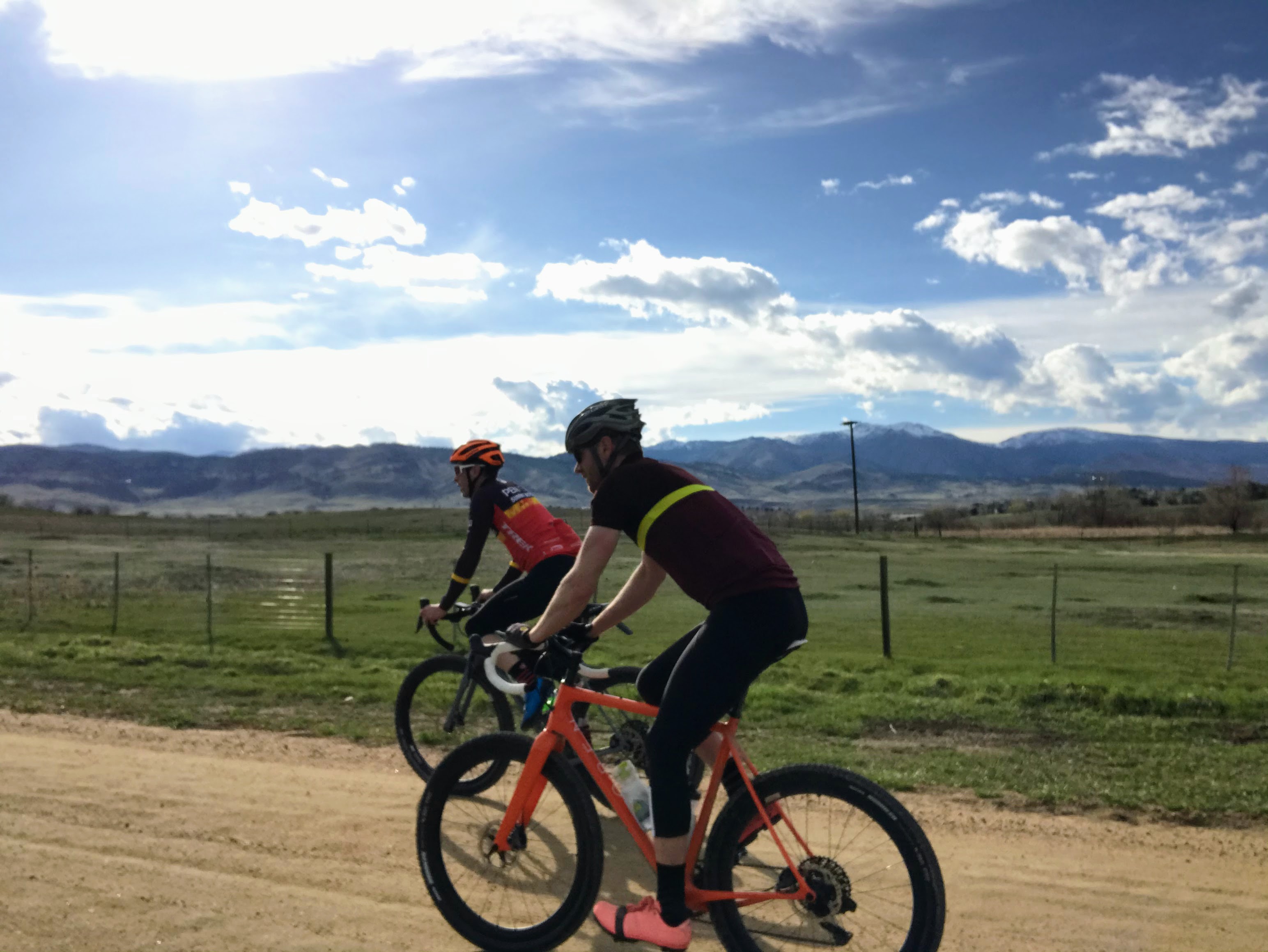 Two cyclists riding gravel roads with mountains and dramatic sky